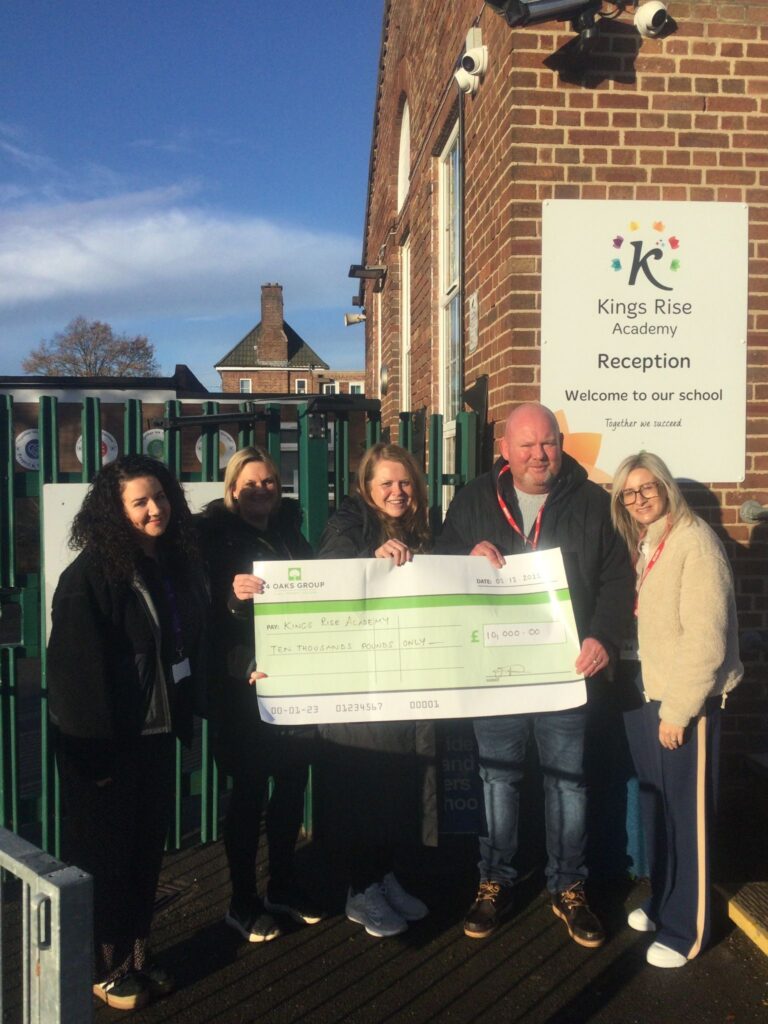 The 4 Oaks Group team standing outside Kings Rise Academy with a giant charity donation check for £10000